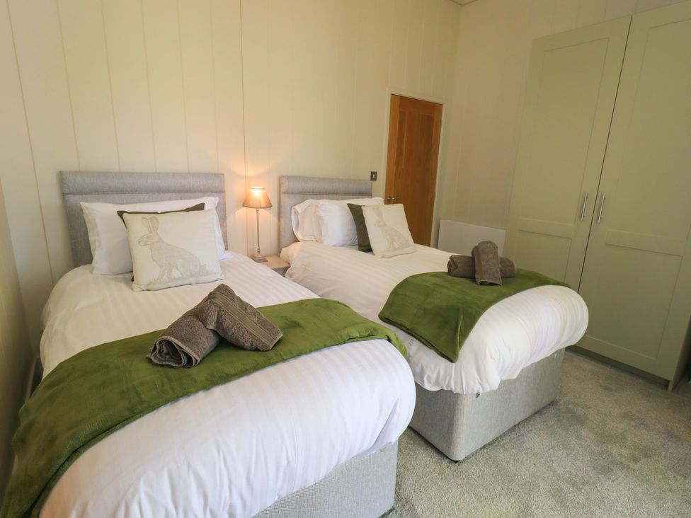 A bedroom with two single beds green throws and folded towels and a wardrobe at Kingfisher Lodge in Gargrave