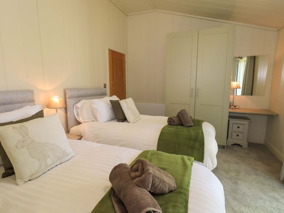 A bedroom with two single beds with green throws and rolled towels a wardrobe and a dressing table with a lamp and mirror at Kingfisher Lodge in Gargrave