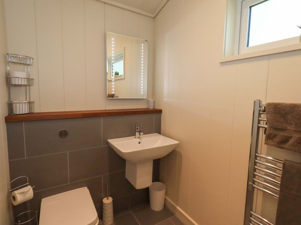 A bathroom with a toilet sink mirror towel rack and window at Kingfisher Lodge in Gargrave
