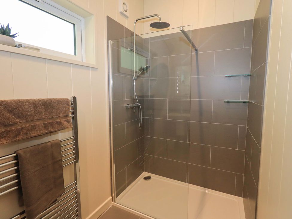 A bathroom with a walk-in shower with grey tiled walls and a glass partition at Kingfisher Lodge in Gargrave