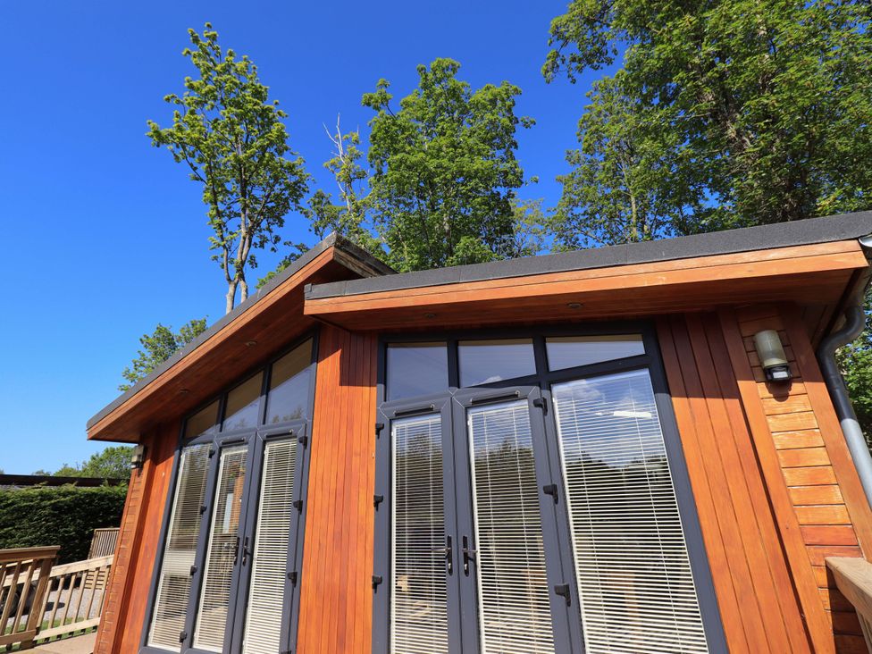 Exterior of a wooden building with large windows and blinds surrounded by trees at Kingfisher Lodge in Gargrave
