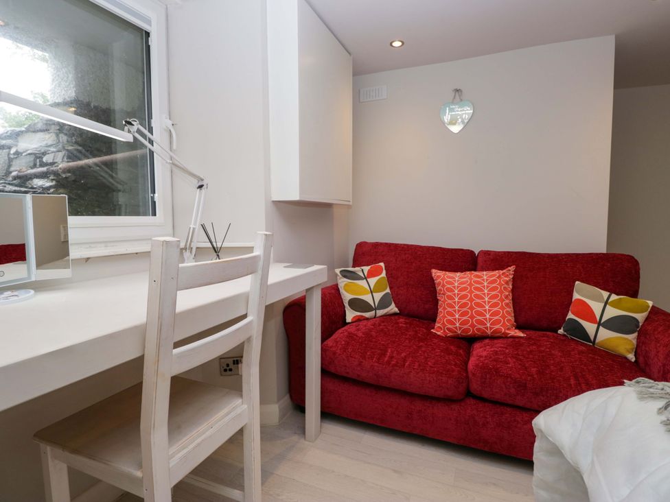 A living room with a red sofa and a desk at Poppy Cottage in Bowness-On-Windermere