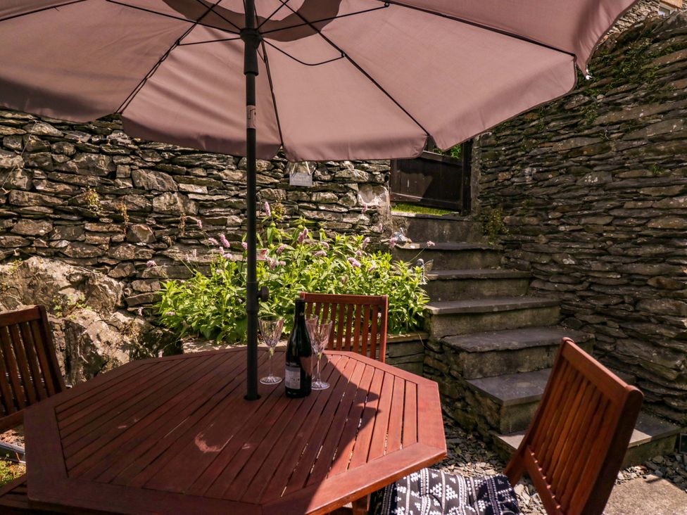 A patio area with a table and chairs under an umbrella at Poppy Cottage in Bowness-On-Windermere
