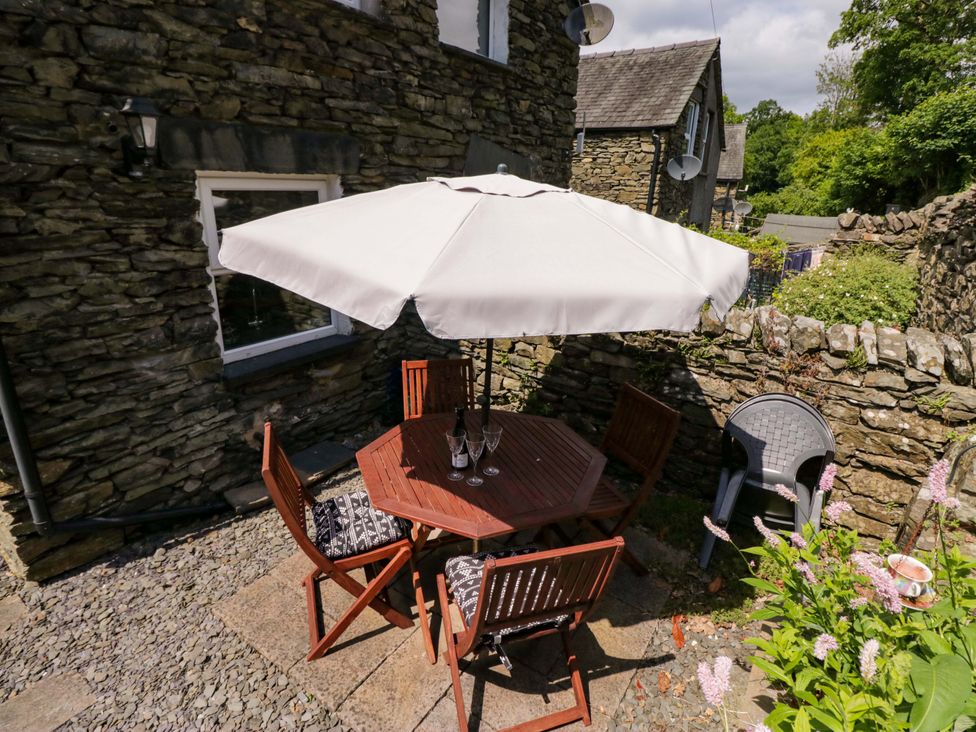 An outdoor area with a wooden table and chairs under an umbrella at Poppy Cottage in Bowness-On-Windermere