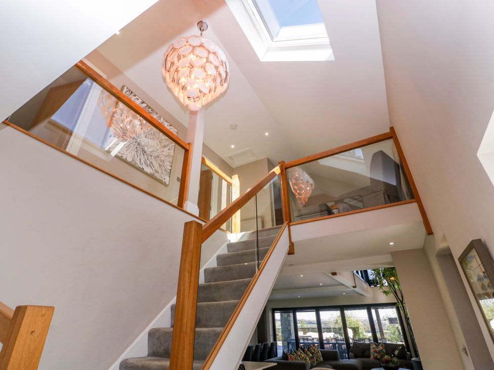A staircase with a chandelier and glass railing at Forest Lodge in Pontyclun