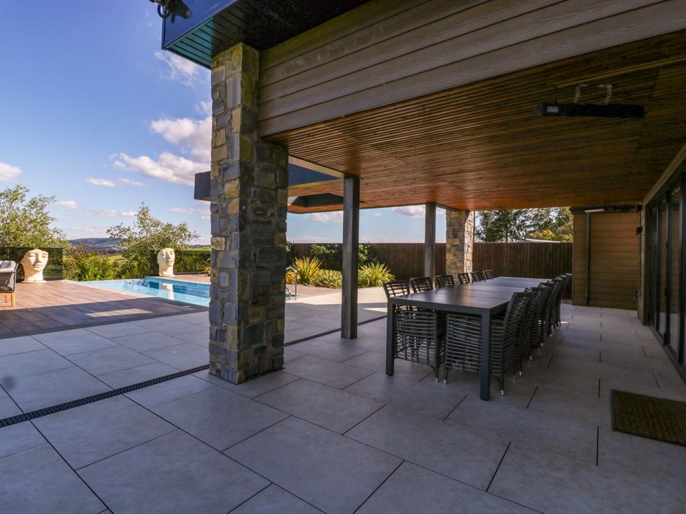 An outdoor patio with a pool and dining table at Forest Lodge in Pontyclun