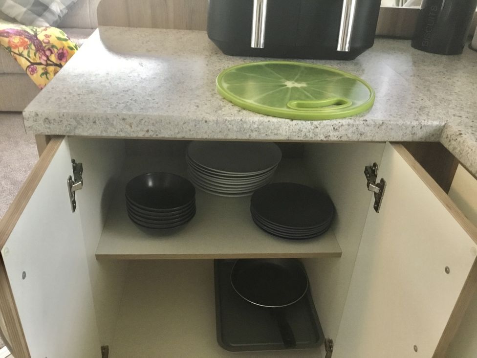 A kitchen countertop with a cutting board and plates in a cabinet at 38 The Green