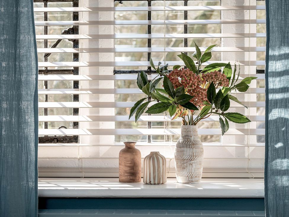 A living room with vases and flowers on a windowsill at East Lodge in Peterborough
