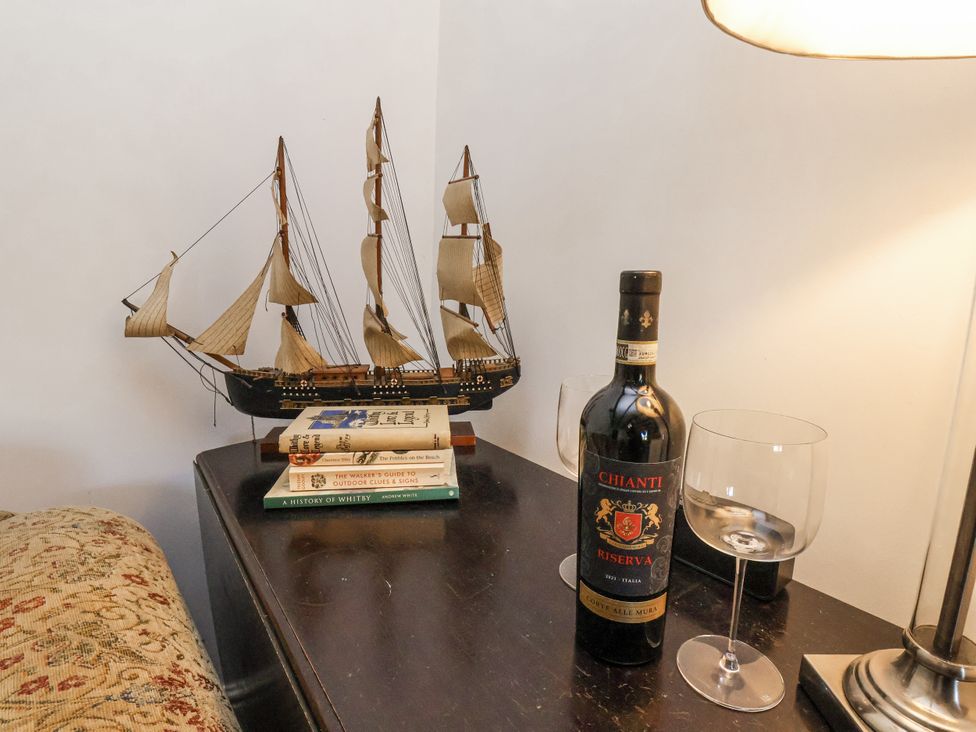 A living room with a model ship, wine bottle, wine glass and books at Rigg Cottage in Sandsend