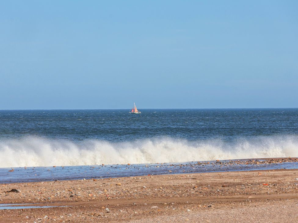 A beach with waves and a sailing boat on the ocean at Rigg Cottage, Mount Pleasant Sandsend