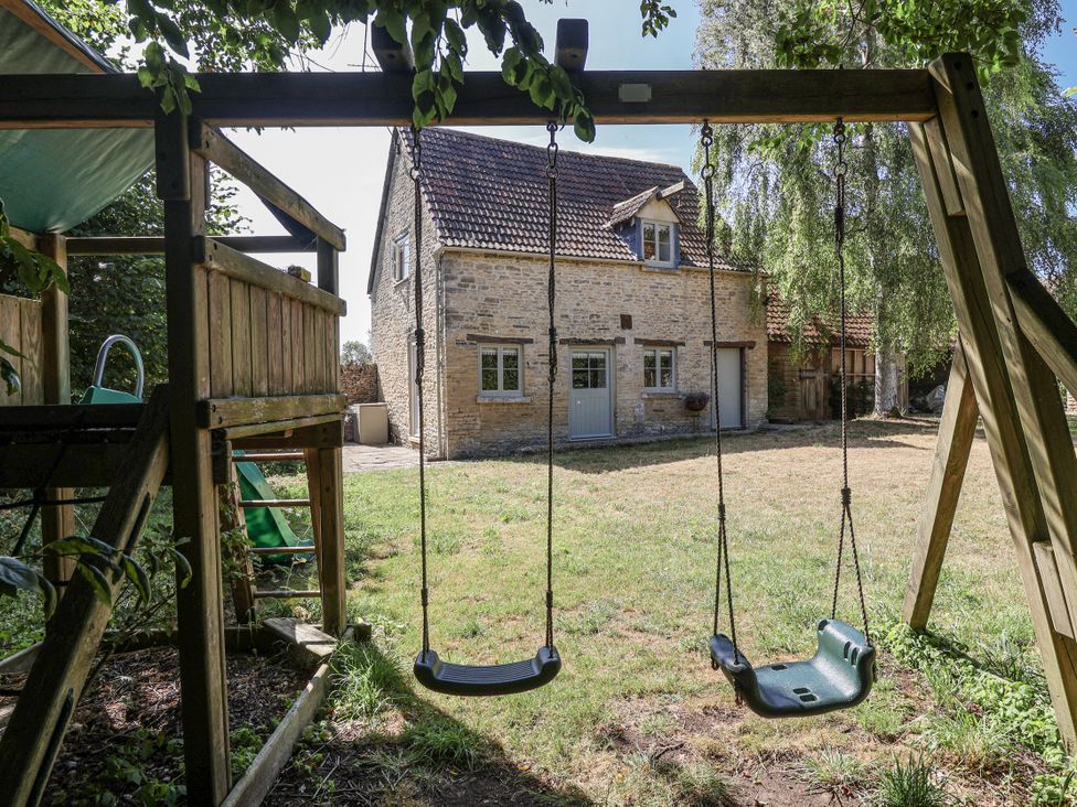 A swing set and playhouse in a garden at Stable cottage Sopworth near Sherston