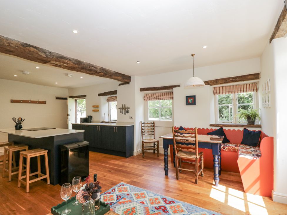 A kitchen with a table, stools and a window at Stable cottage in Sopworth near Sherston
