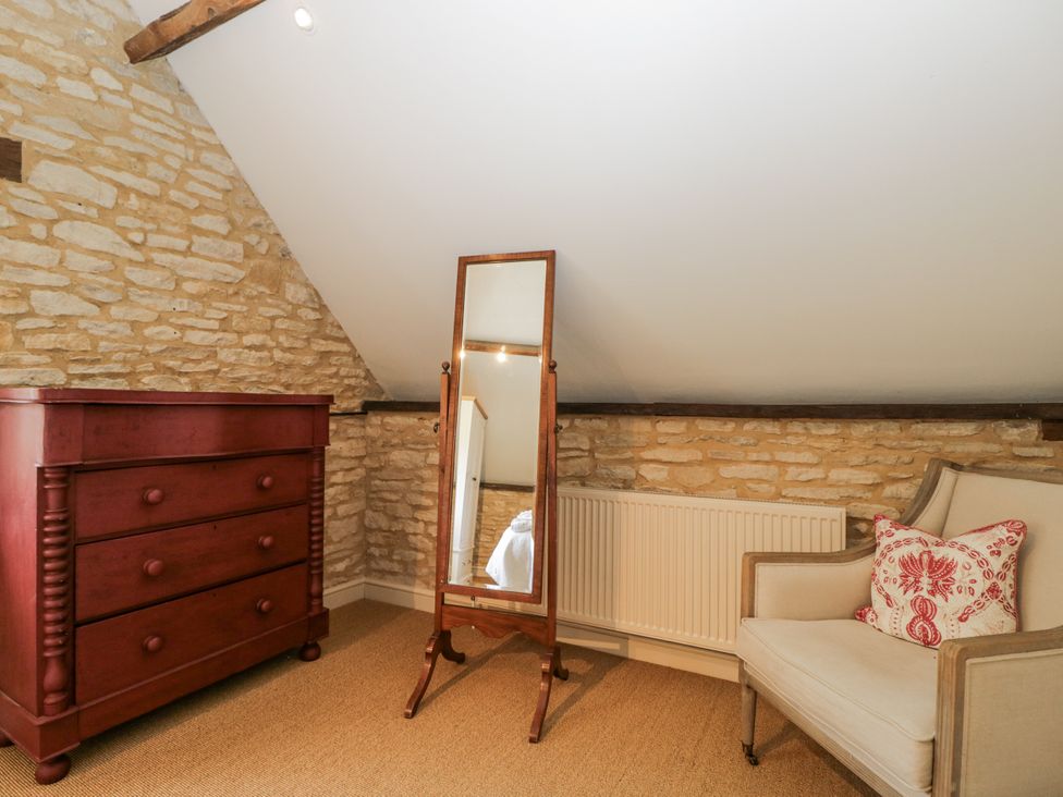 A bedroom with a dresser, mirror, and chair at Stable cottage in Sopworth near Sherston