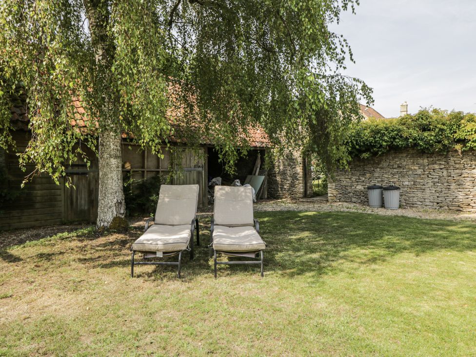 A garden with deck chairs and a stone wall at Stable cottage in Sopworth near Sherston