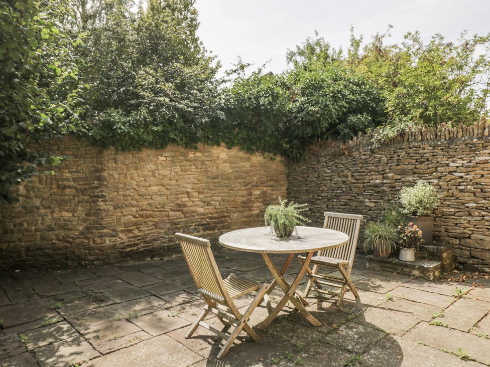 A garden with a stone wall and a table with chairs at Stable cottage Sopworth near Sherston