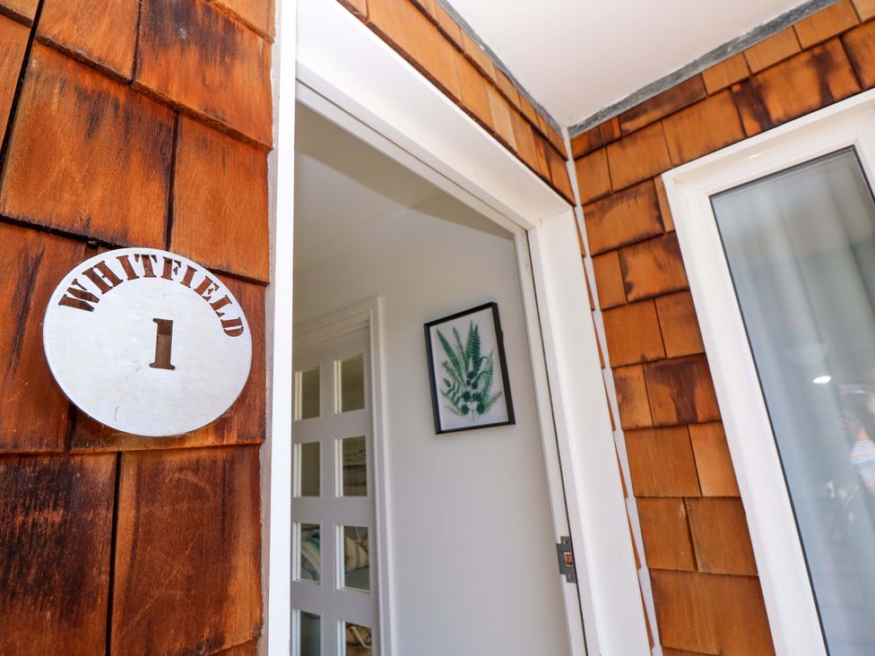 Entrance door with white frame on brown wooden shingle wall and a round sign reading Whitfield 1 in Yarmouth
