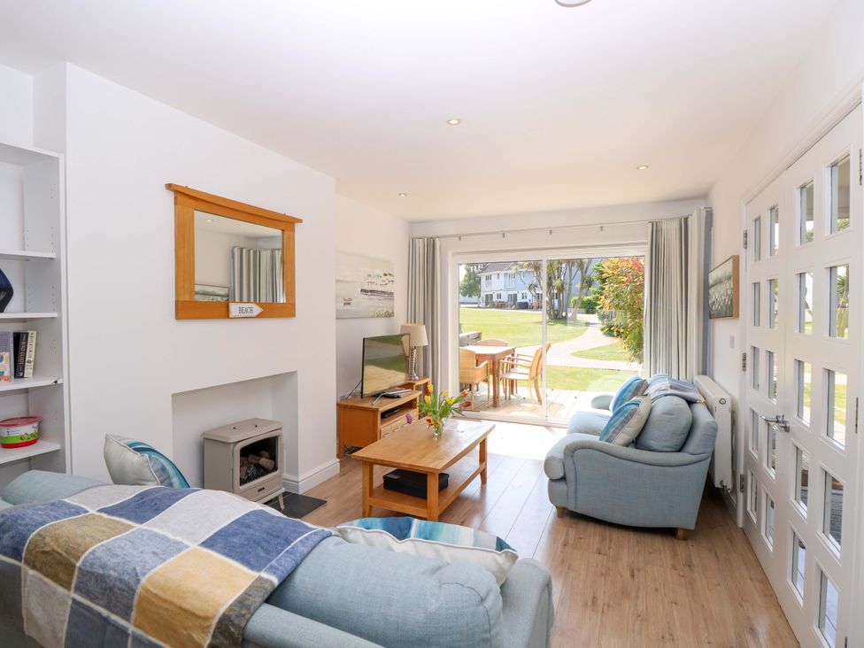A living room with two blue sofas a wooden coffee table a TV on a wooden stand a wood stove and glass doors leading to a garden at Whitfield P1 in Yarmouth