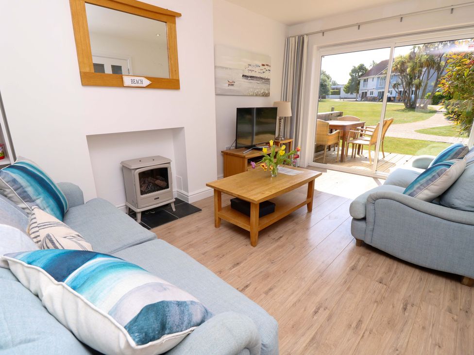 A living room with two blue sofas a wooden coffee table a flat screen tv and sliding glass doors leading to an outdoor seating area at Whitfield P1 in Yarmouth