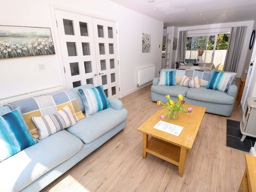 A living room with two blue sofas a wooden coffee table with flowers and a dining area with a sliding door at Whitfield P1 in Yarmouth