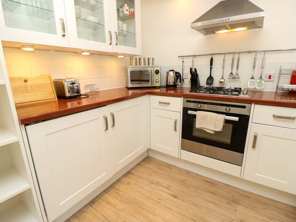 A kitchen with white cabinets wooden countertops a gas stove an oven microwave kettle and kitchen utensils hanging on a rod at Whitfield P1 in Yarmouth