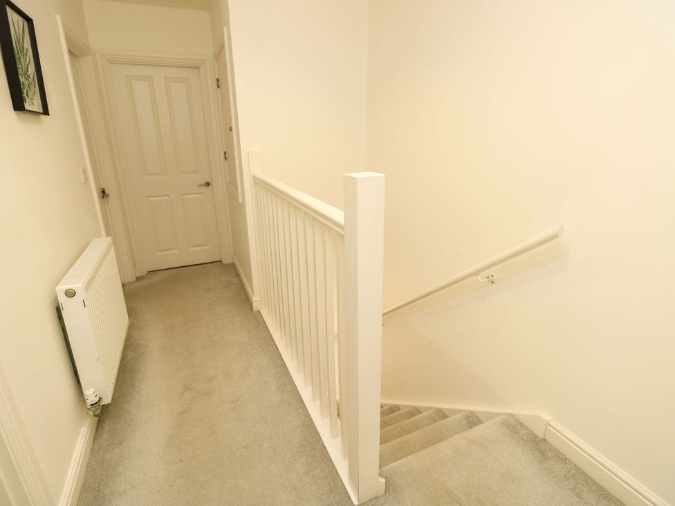 A hallway with a closed door radiator artwork and stairs with a handrail at Whitfield P1 in Yarmouth