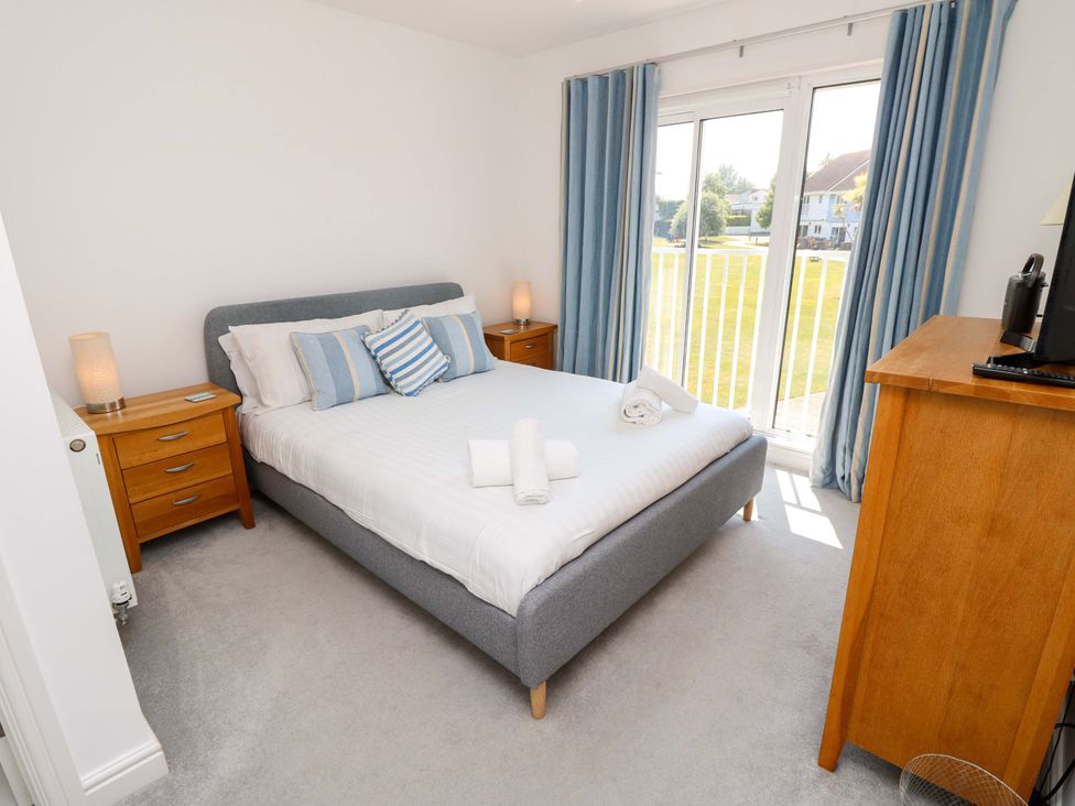 A bedroom with a grey bed frame white bedding blue striped pillows wooden bedside tables and a wooden chest of drawers with a window and blue curtains at Whitfield P1 in Yarmouth