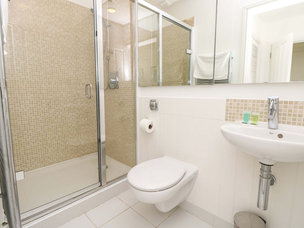 A bathroom with a shower enclosure, wall-mounted toilet, and a sink with toiletries at Whitfield P1 in Yarmouth