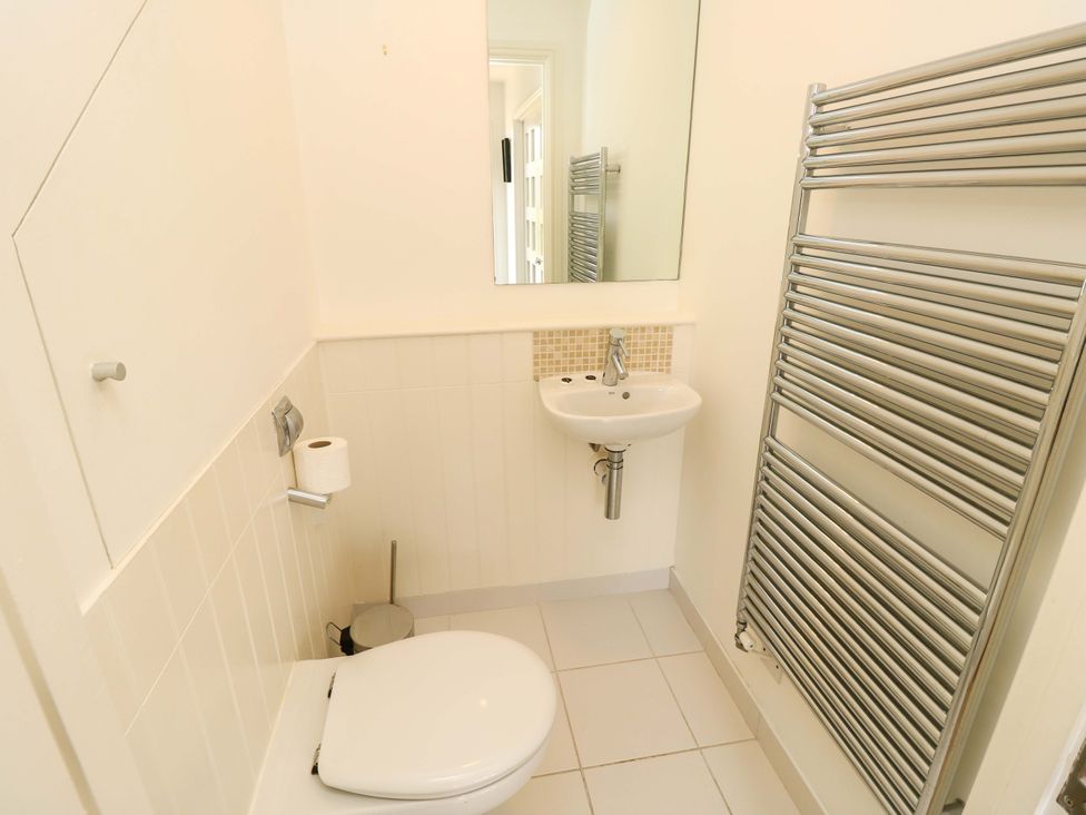 A small bathroom with a toilet, wall-mounted sink, rectangular mirror, toilet paper holder, and a metal towel radiator at Whitfield P1 in Yarmouth