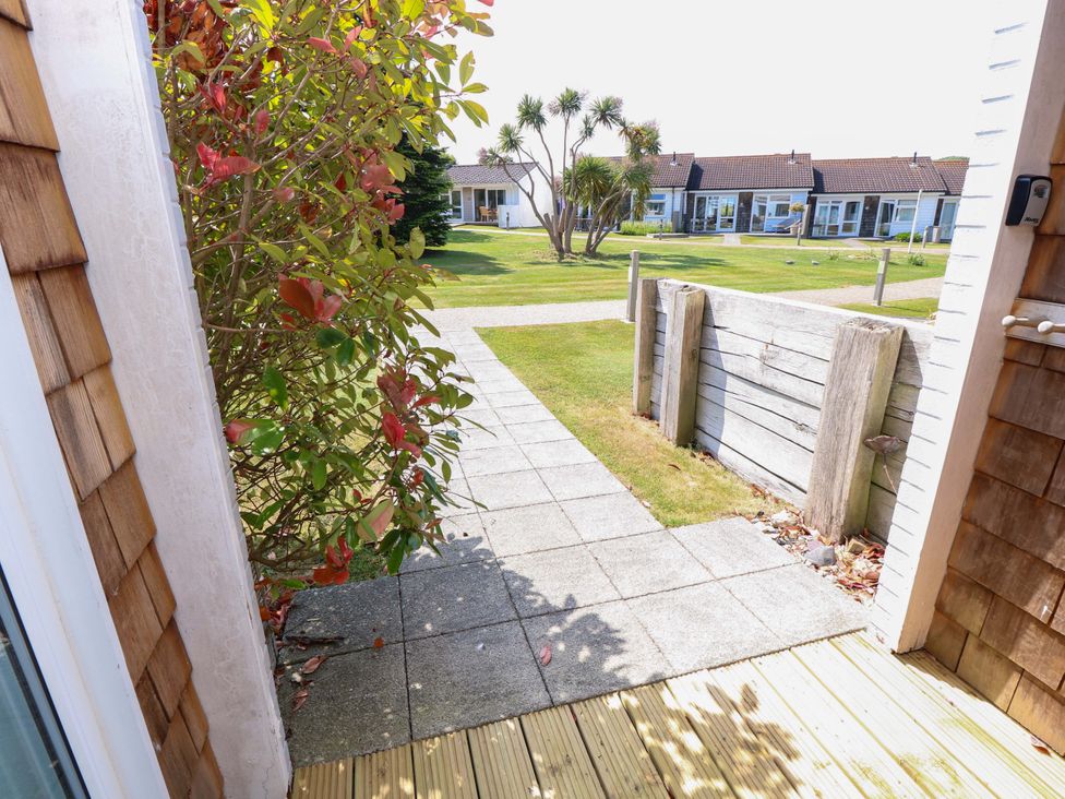 A view from a doorway showing a paved path leading to a grassy area with palm trees and small buildings at Whitfield P1 in Yarmouth
