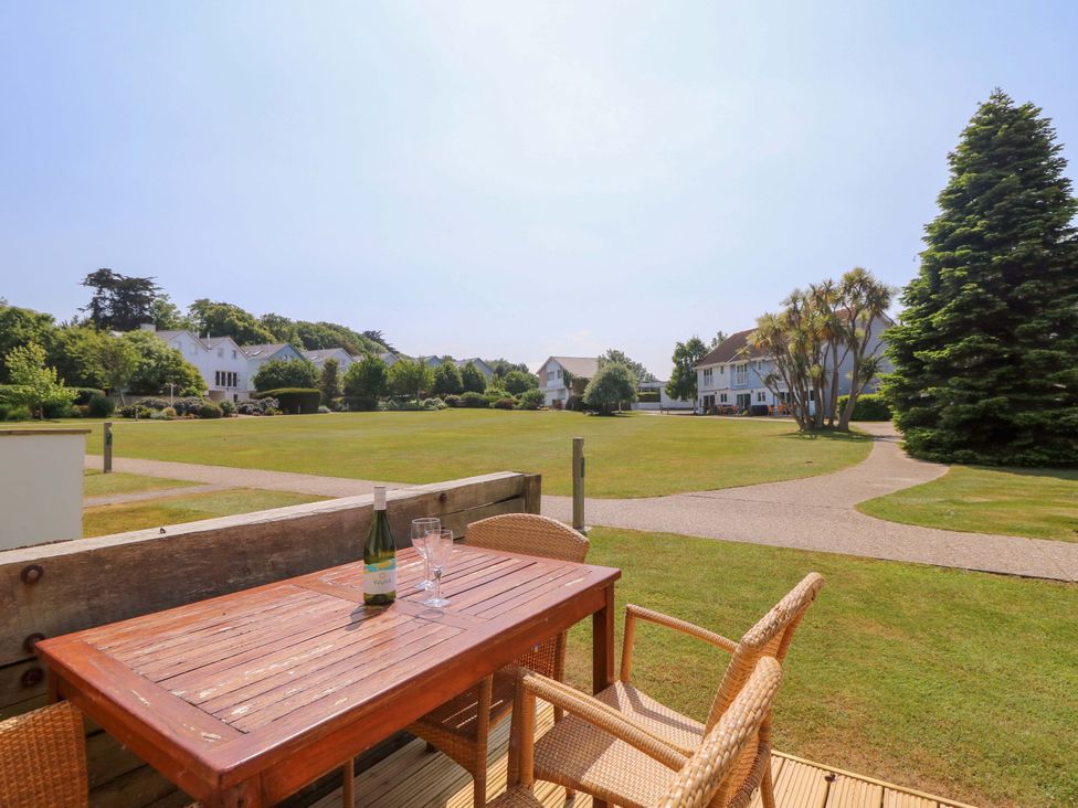 An outdoor wooden table with a bottle and glasses on a deck overlooking grassy lawns and houses at Whitfield P1 in Yarmouth