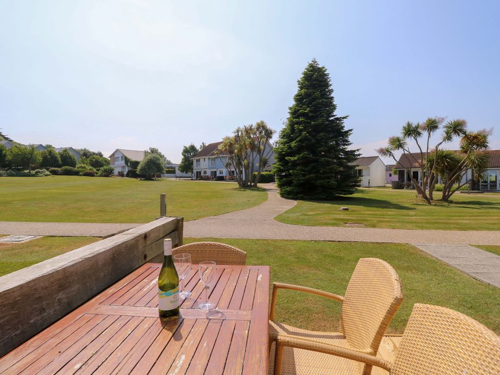 An outdoor wooden table with a bottle of wine and glasses on a lawn with houses and trees in the background at Whitfield P1 in Yarmouth