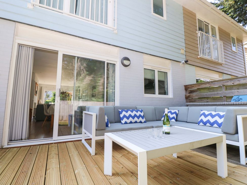 An outdoor patio with a wooden deck sofa with blue and white pillows and a white table with a bottle and glasses at Whitfield P1 in Yarmouth
