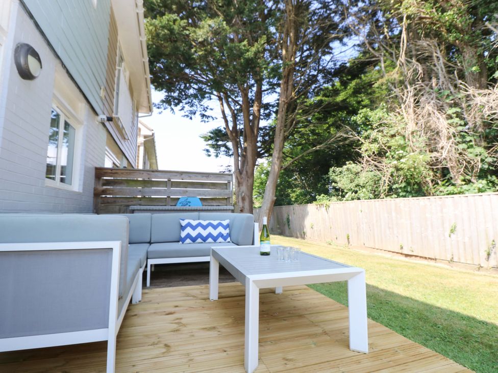An outdoor patio with a gray sectional sofa a white table with a wine bottle and glasses wooden deck and trees at Whitfield P1 in Yarmouth