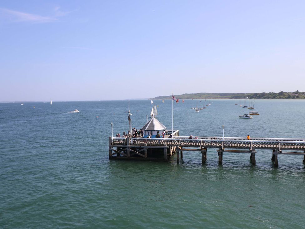 A wooden pier extending into the sea with boats in the water and people walking on the pier at Whitfield P1 in Yarmouth