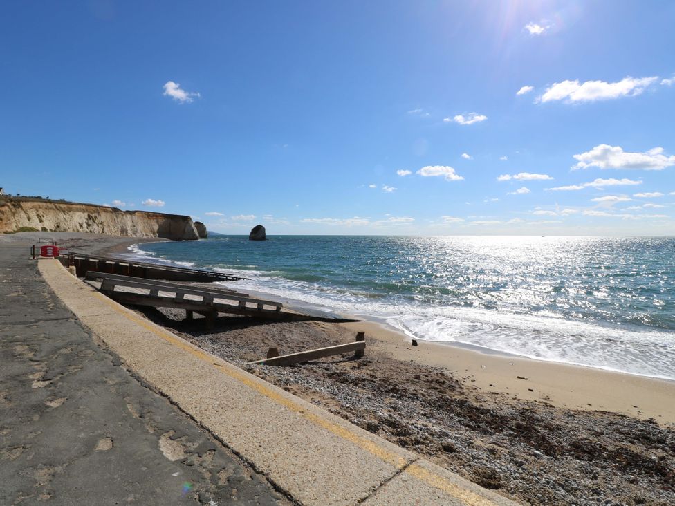 A beach with a concrete promenade wooden groynes and cliffs in the background at Whitfield P1 in Yarmouth