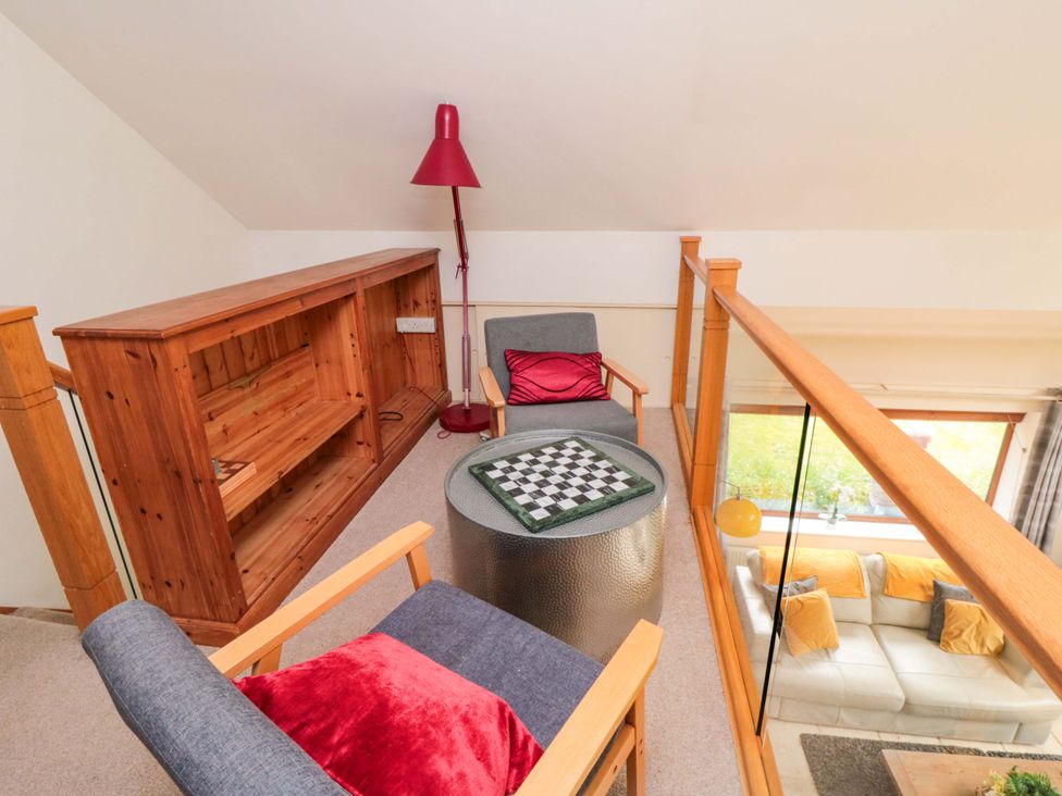 A loft area with a bookshelf, lamp, chairs, and a table at Lawnswood