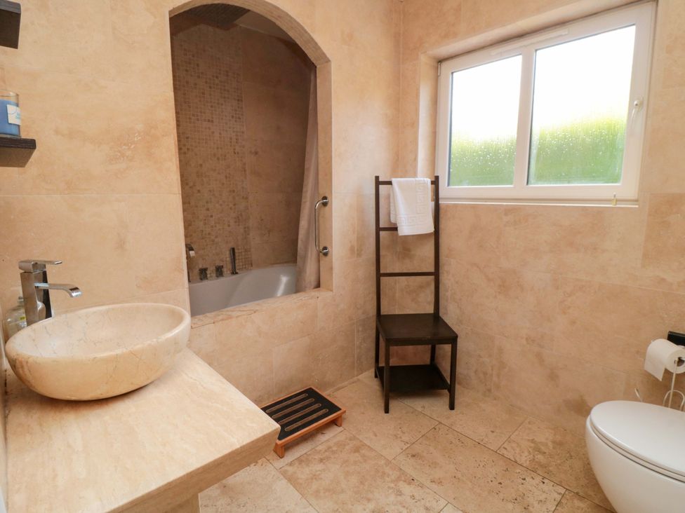 A bathroom featuring a bath tub, toilet, sink, and chair at Lawnswood