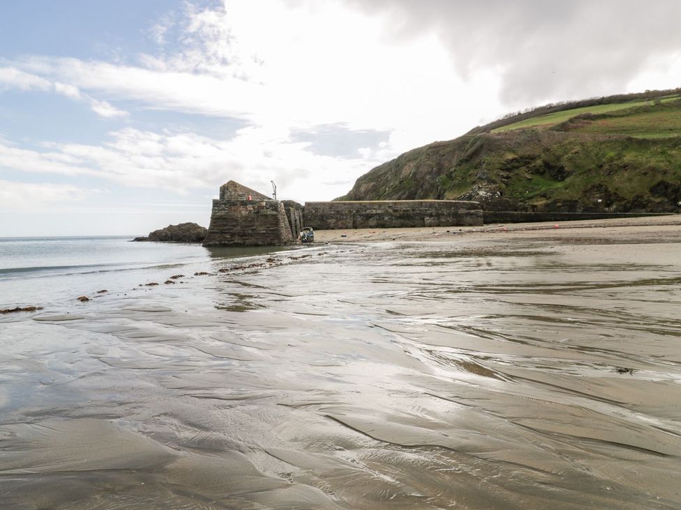 A beach with a pier and cliffs at Sunset Cottage in Gorran Churchtown