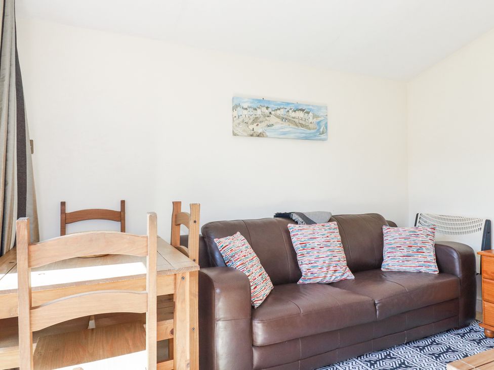 A dining table with wooden chairs next to a brown leather sofa with three cushions at 101 Atlantic Bays Holiday Park in Padstow