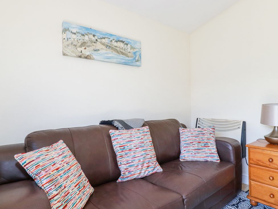 A brown leather sofa with three colorful patterned cushions in a living room with a wooden side table and lamp at 101 Atlantic Bays Holiday Park in Padstow