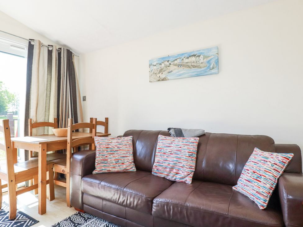 A living room with a brown leather sofa and colorful cushions next to a wooden dining table with chairs at 101 Atlantic Bays Holiday Park in Padstow