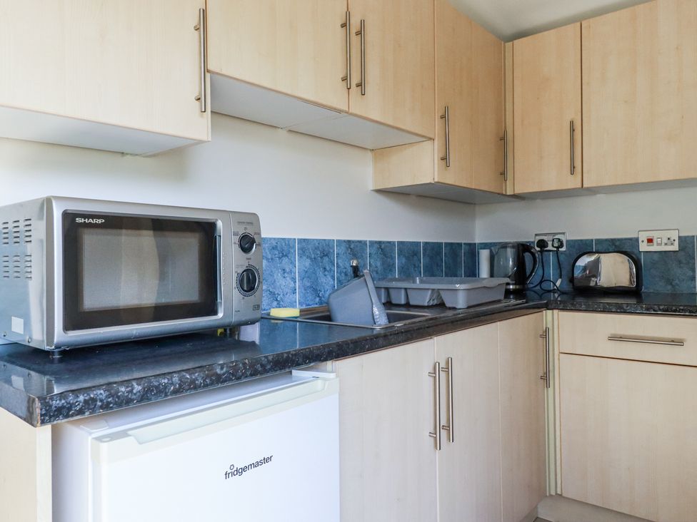 A kitchen with a microwave on a countertop and cupboards above and below the counter at 101 Atlantic Bays Holiday Park in Padstow