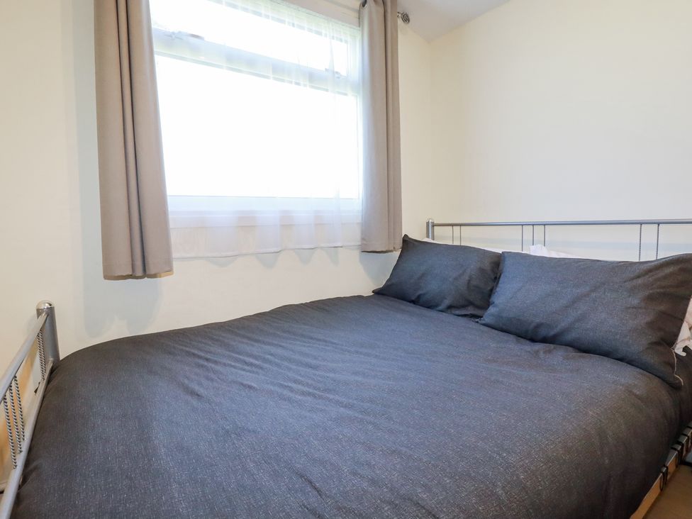 A bedroom with a metal bed frame gray bedding and a window with curtains at 101 Atlantic Bays Holiday Park in Padstow