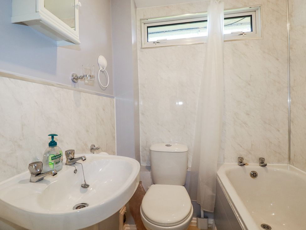 A small bathroom with a sink, toilet, bathtub with shower curtain, and a small window at 101 Atlantic Bays Holiday Park in Padstow