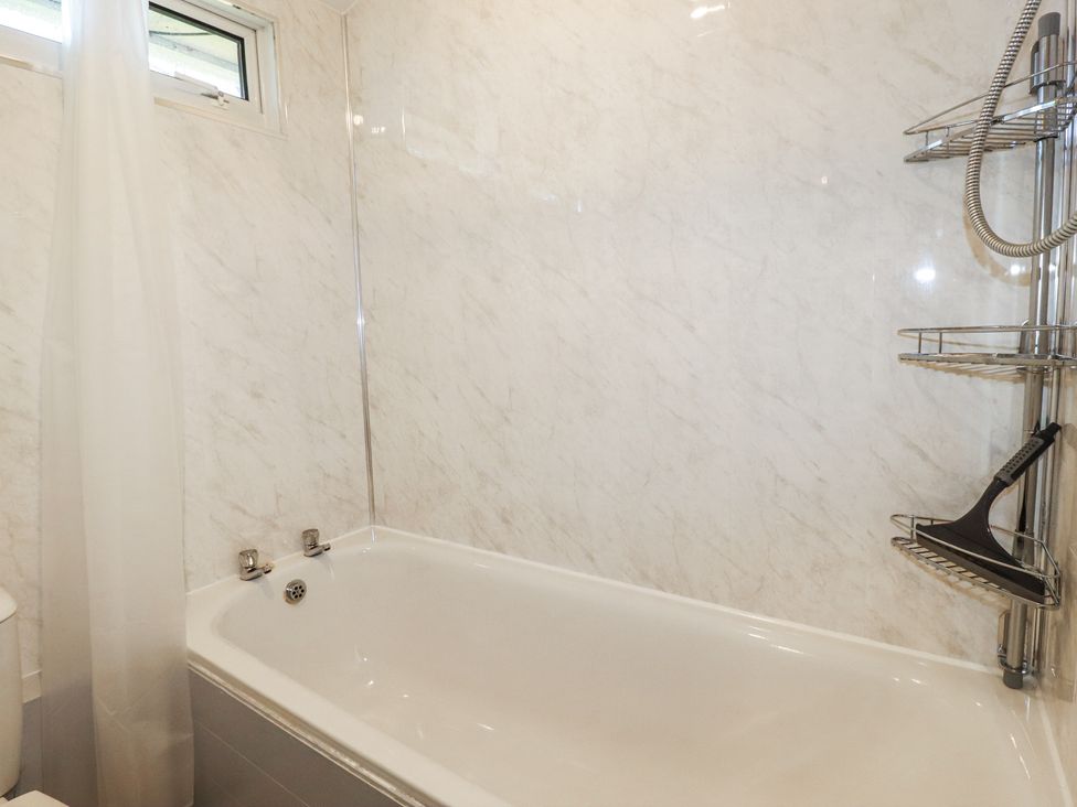 A bathroom with a white bathtub shower curtain and a metal shower caddy with a squeegee at 101 Atlantic Bays Holiday Park Padstow