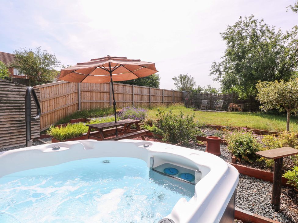 A garden with a hot tub, umbrella, table, and chairs at 3 Birkbeck Way Norwich