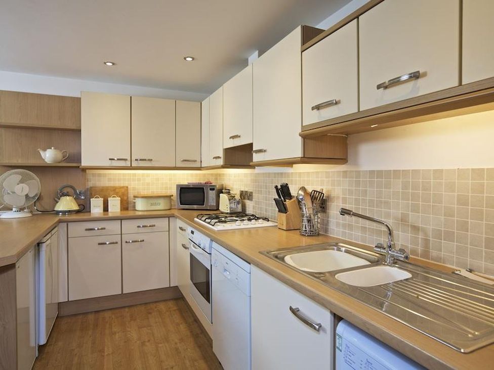 A kitchen with white cabinets a sink a stove a microwave and kitchen utensils at 10 Dartmouth House in Dartmouth