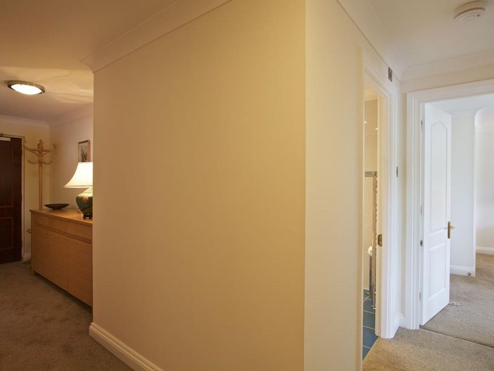A hallway with a wooden cabinet lamp and coat stand and doors leading to other rooms at 10 Dartmouth House in Dartmouth