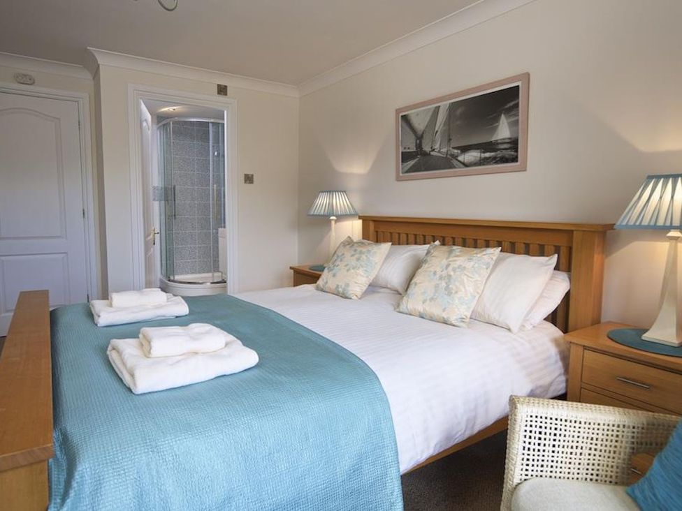 A bedroom with a double bed blue bedspread and pillows two bedside tables with lamps and an ensuite shower at 10 Dartmouth House in Dartmouth