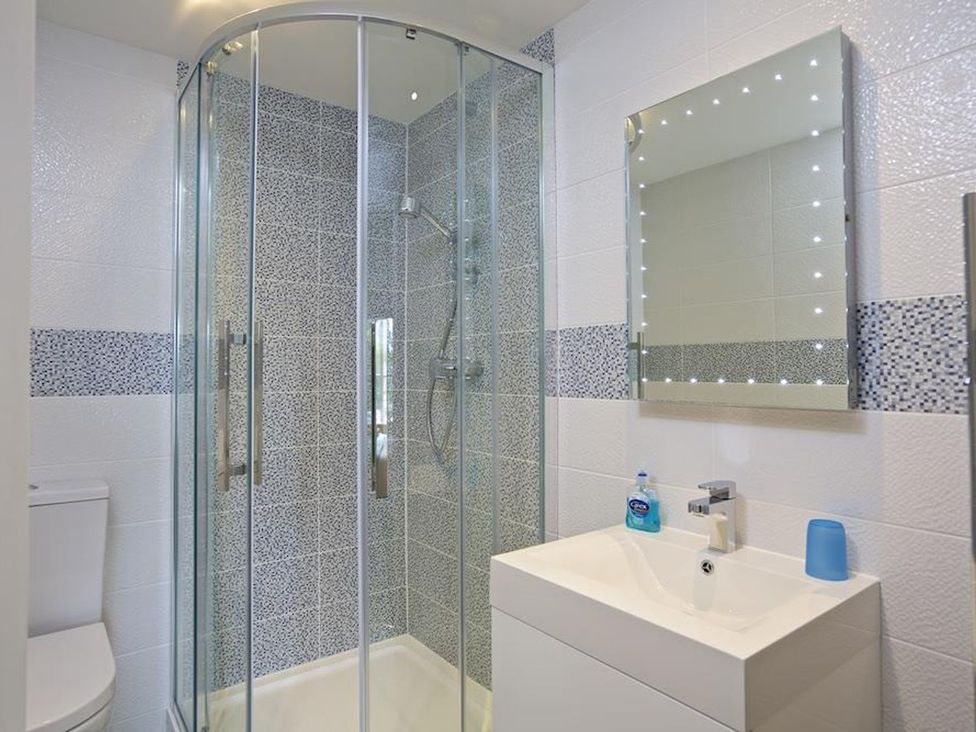 A bathroom with a glass shower enclosure a white sink with a mirror above and a toilet at 10 Dartmouth House in Dartmouth